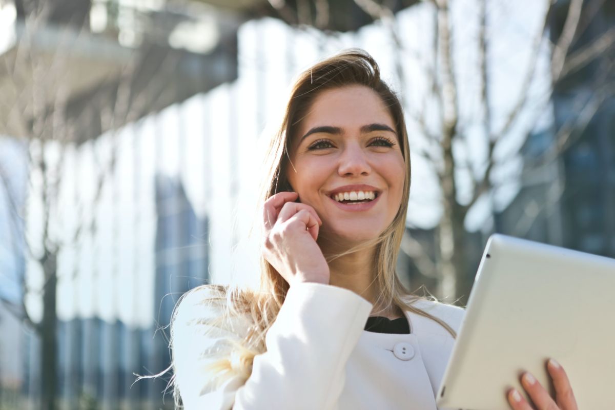 Woman smiling whilst on the phone and holding a tablet with a white jumper